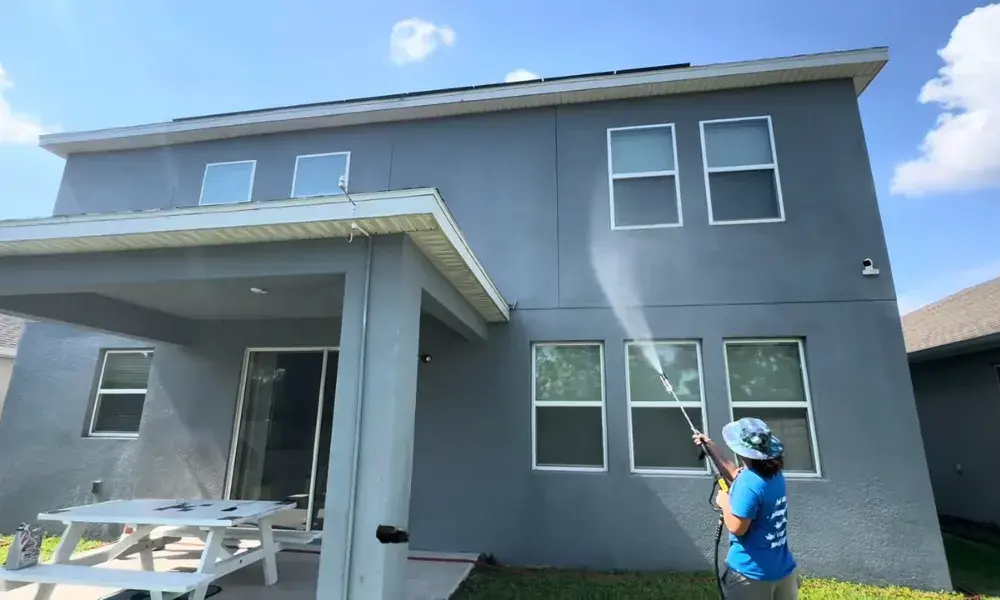 Technician House washing Eugene the exterior of a two-story home using professional soft washing equipment to remove dirt, mold, and algae.